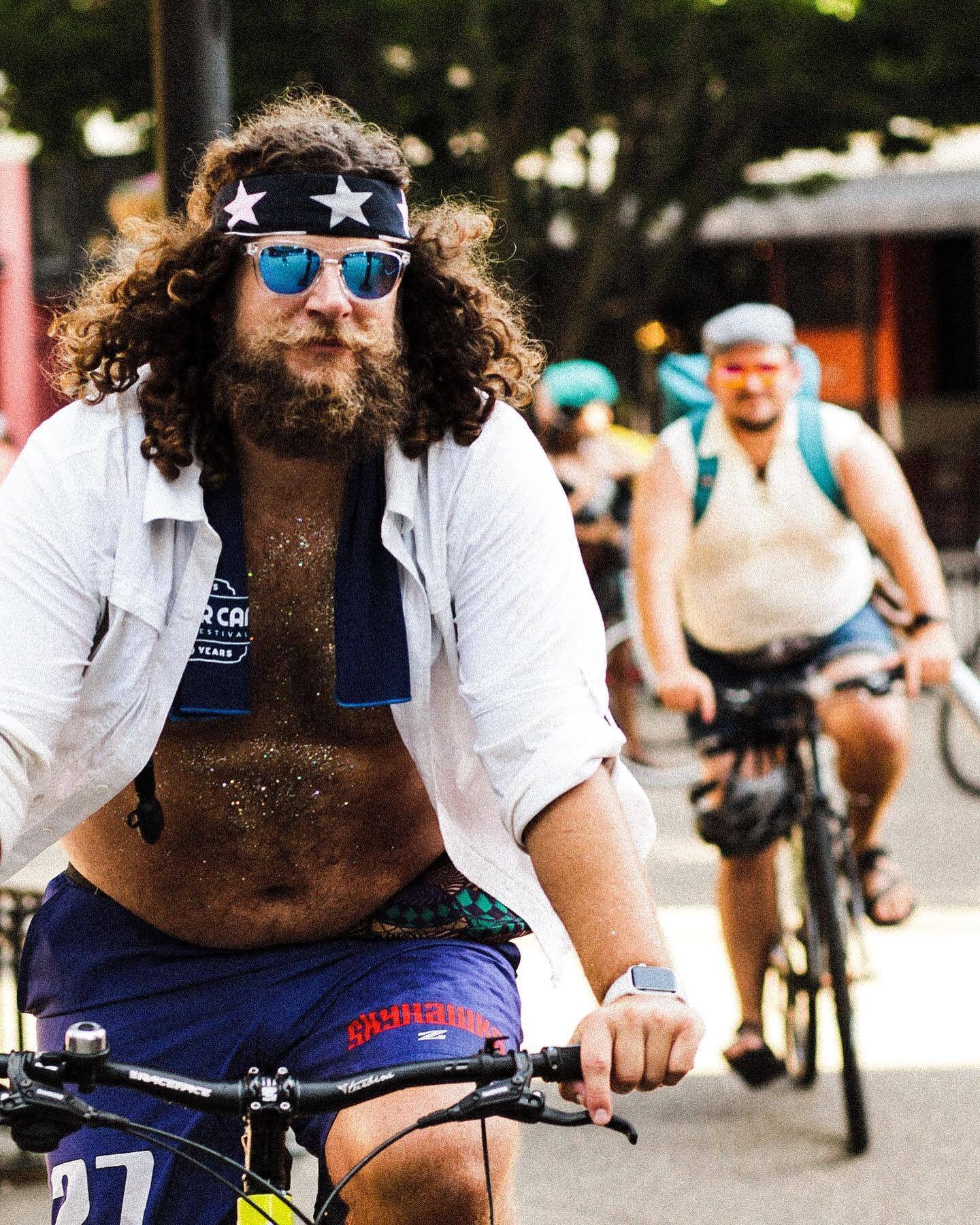 A cyclist in a star-print bandana and mirrored sunglasses rides past in the sun