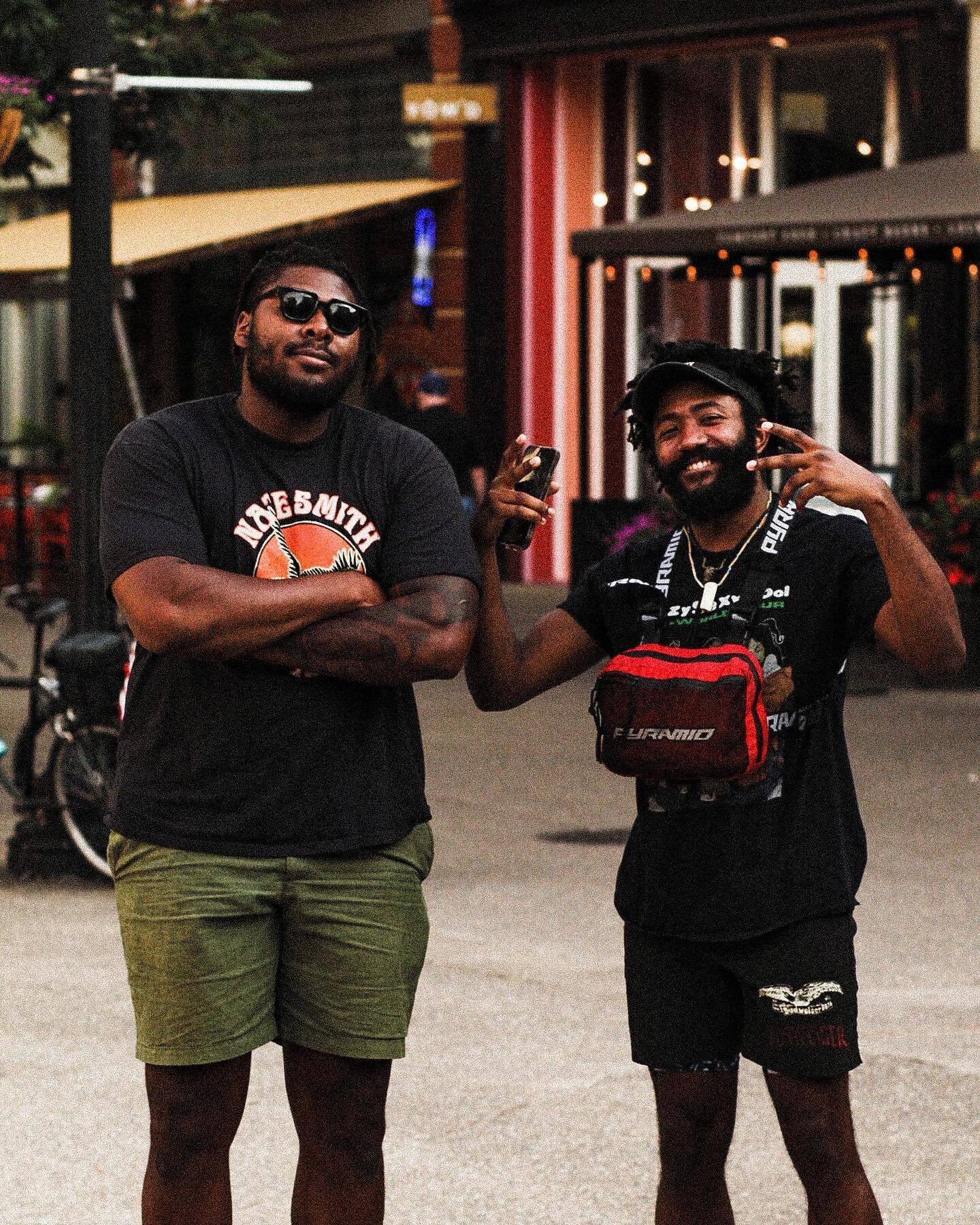 Two men pose for the camera on a downtown sidewalk