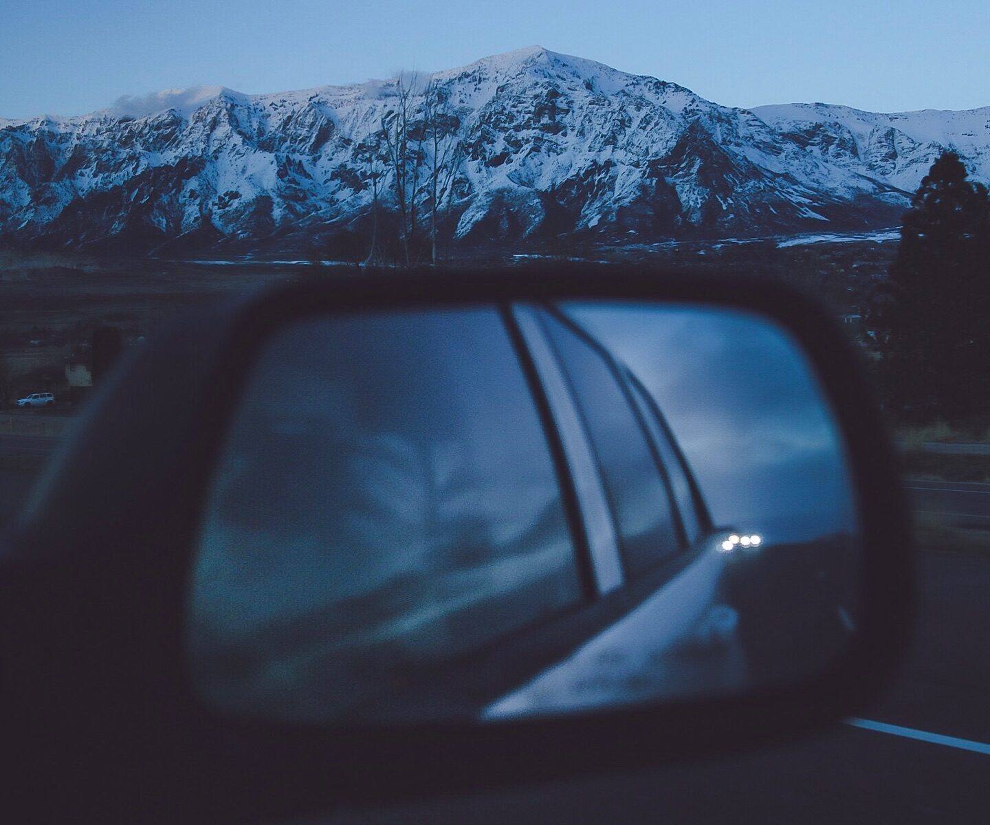 Snowy mountains reflected in a car wing mirror at dusk
