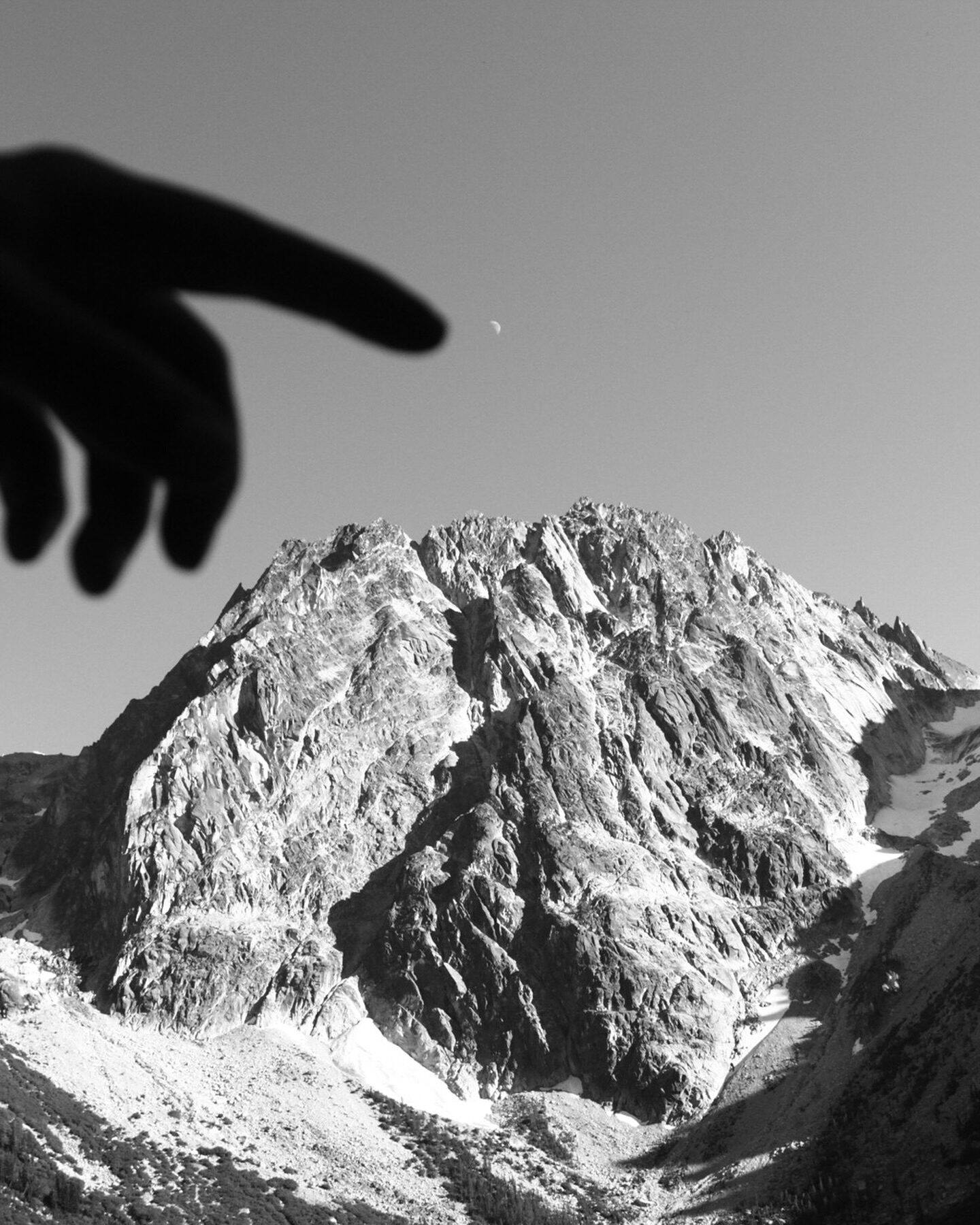 A rocky peak in black and white with a hand reaching into frame