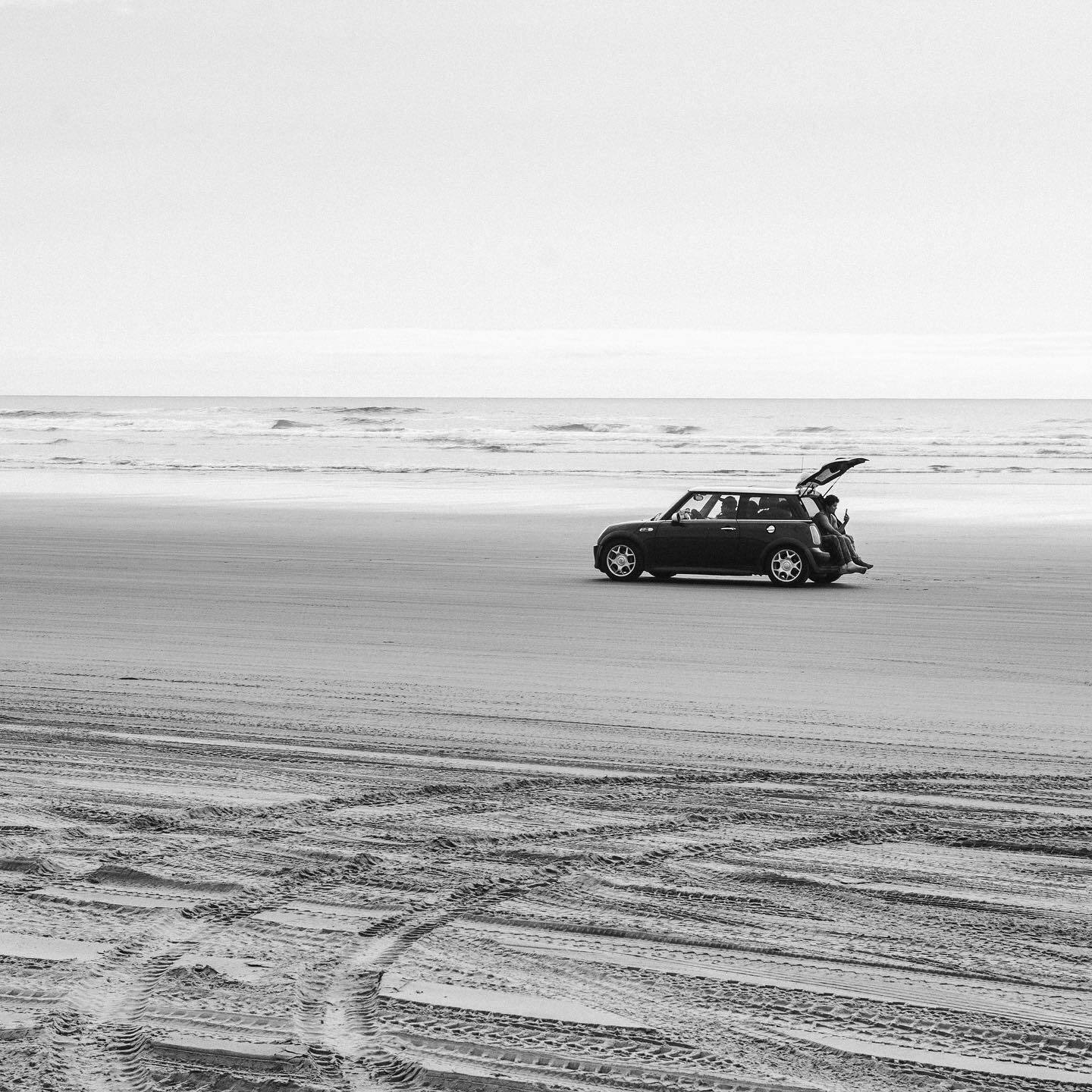 A small car parked on the beach with its boot open
