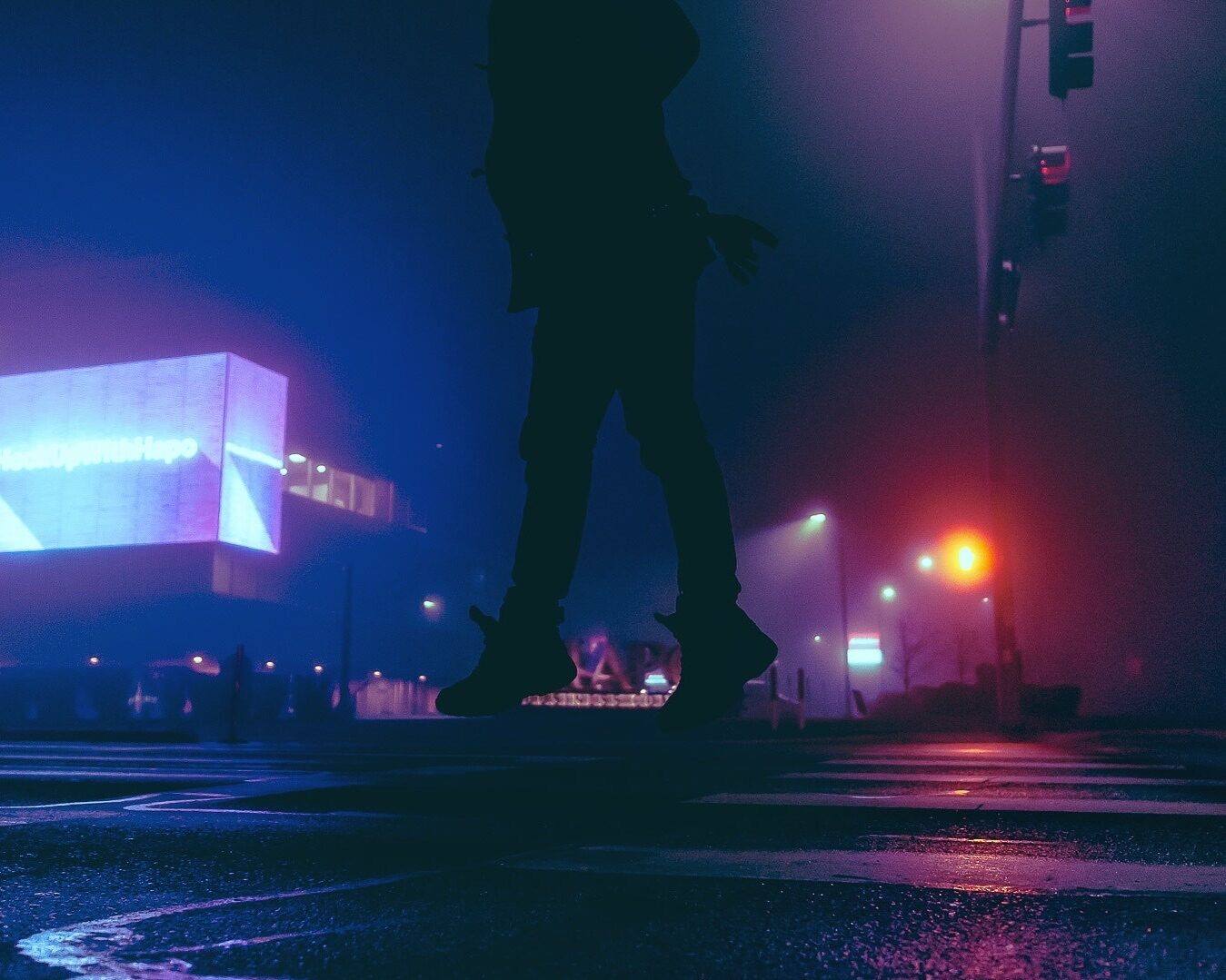 A silhouette crossing a neon-lit street in the rain